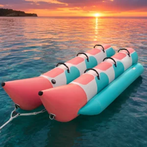 Double inflatable banana boat towable in teal, coral and white with two long rider tubes, black handles and sunset sea background