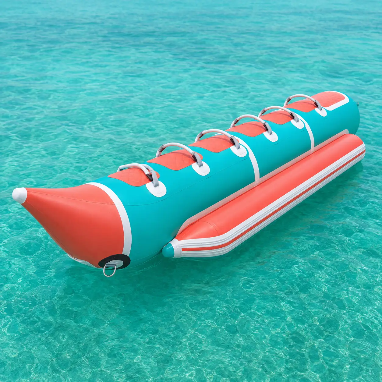 Custom inflatable banana boat in teal, coral and white with multiple rider handles and side float tubes on clear blue water